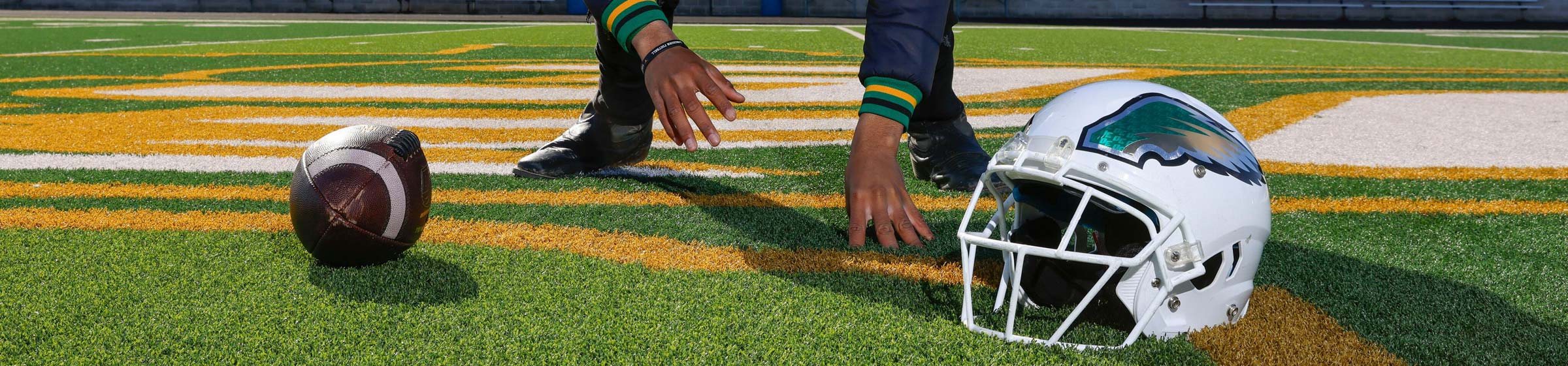 A closeup on a high school football player's hands, football, and helmet.